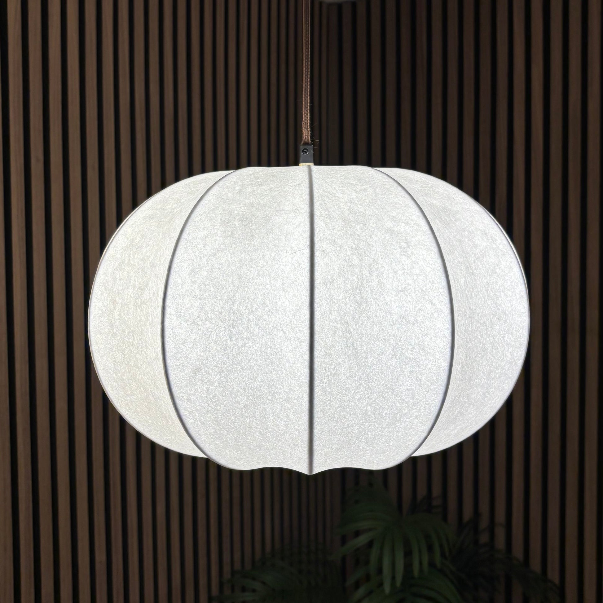 White pendant light hanging in a room with wooden paneling.