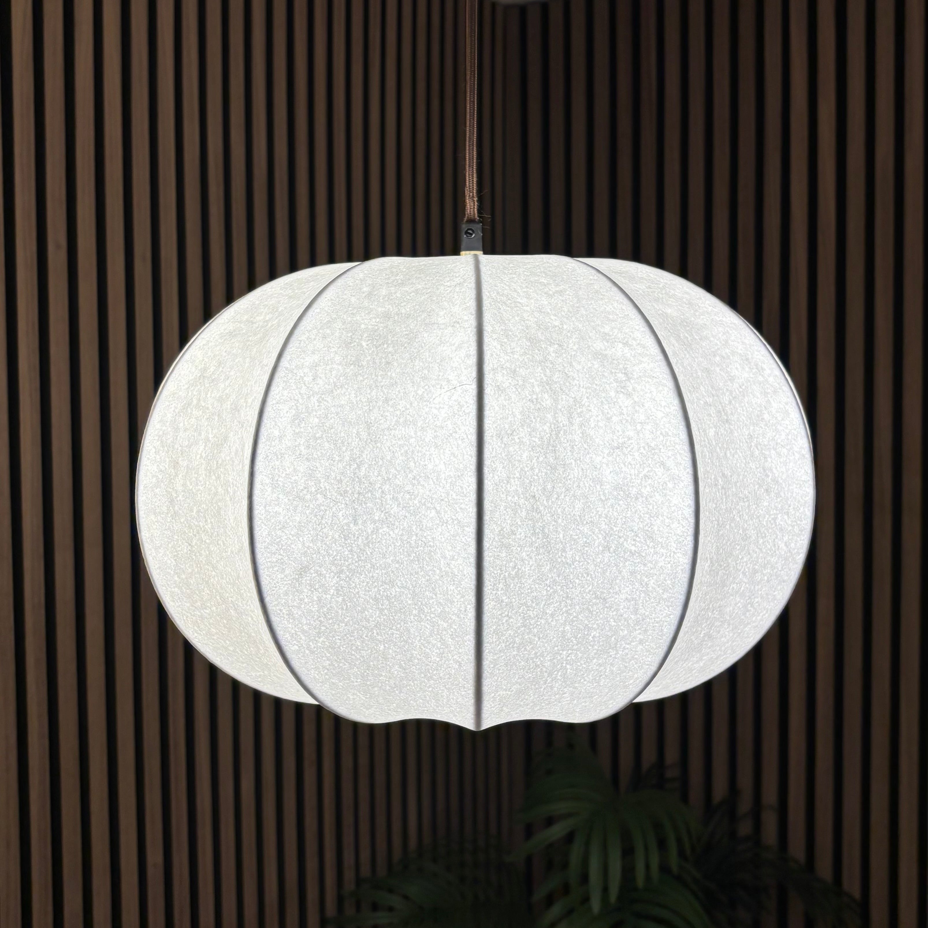 White pendant light hanging in a room with wooden paneling.