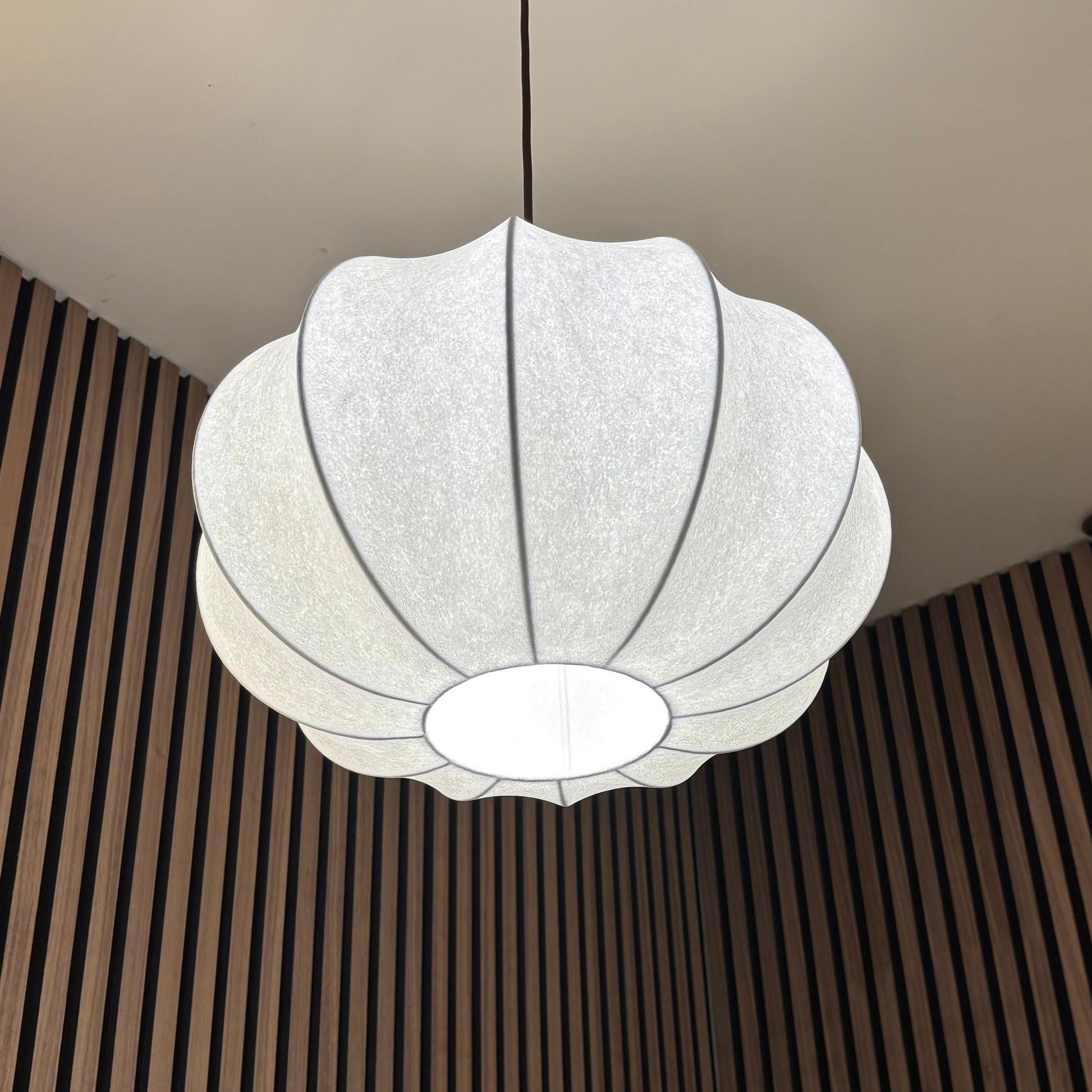 White pendant light hanging from a ceiling with a striped wall in the background