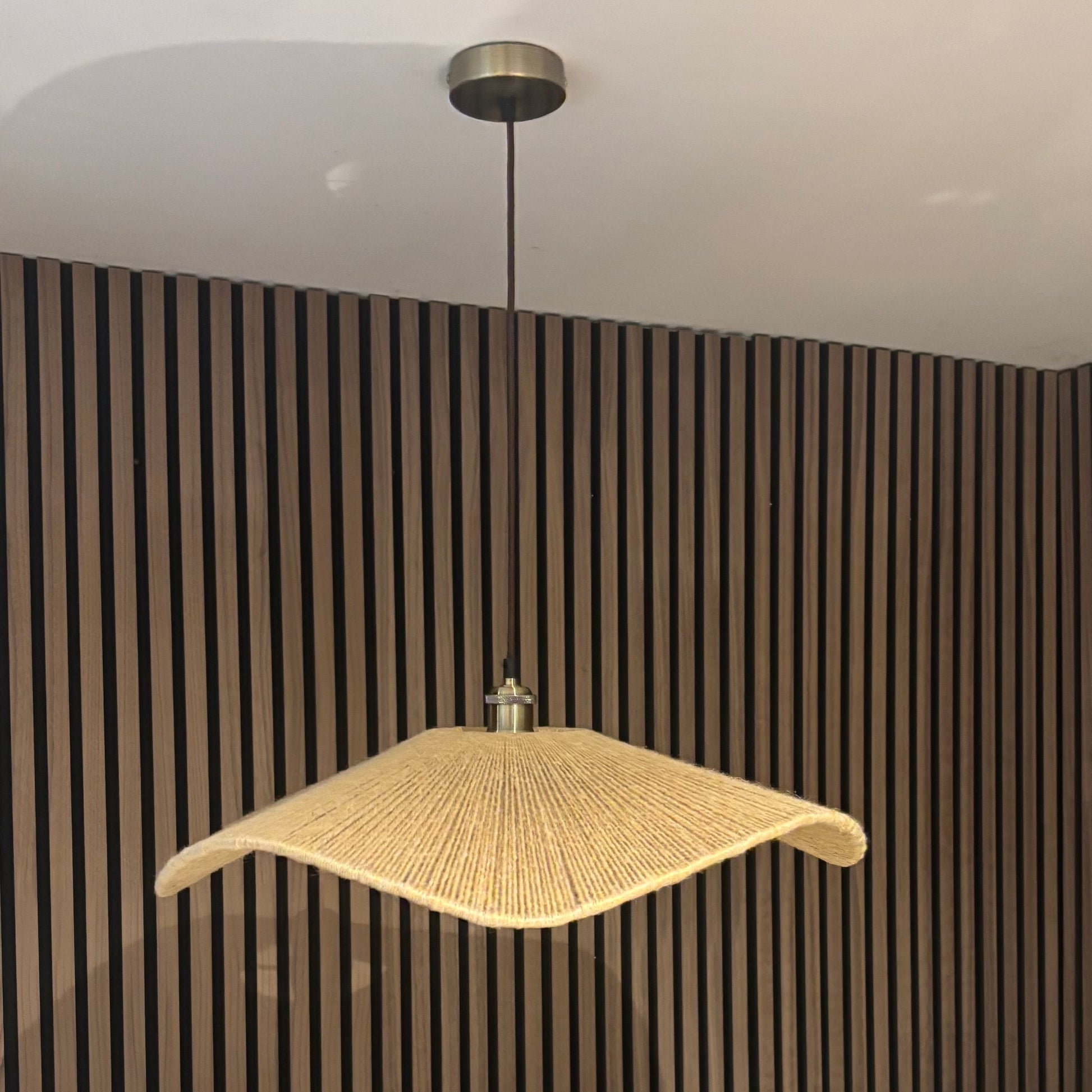 Modern pendant light hanging against a striped wall with a chair and plant in the foreground.