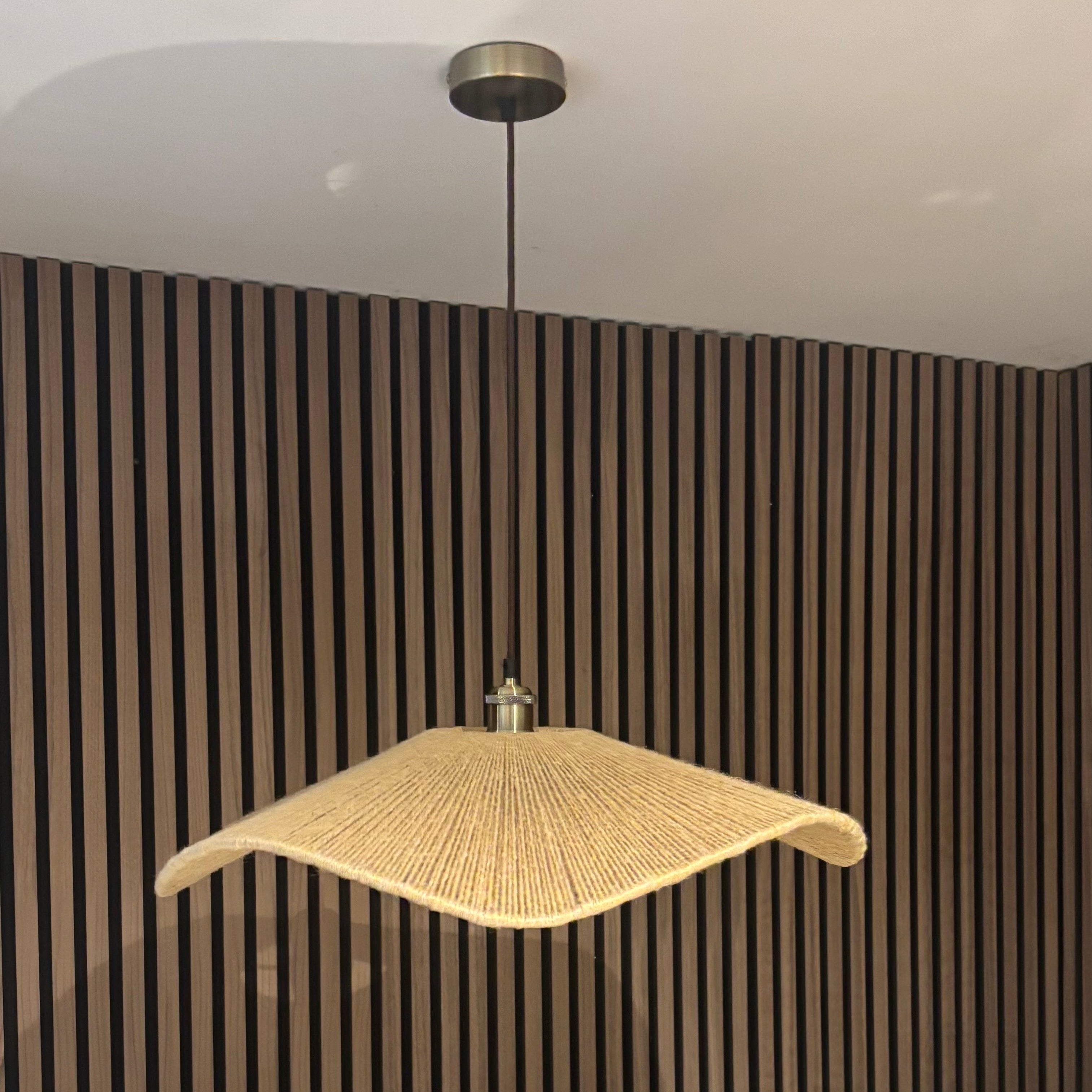 Modern pendant light hanging against a striped wall with a chair and plant in the foreground.