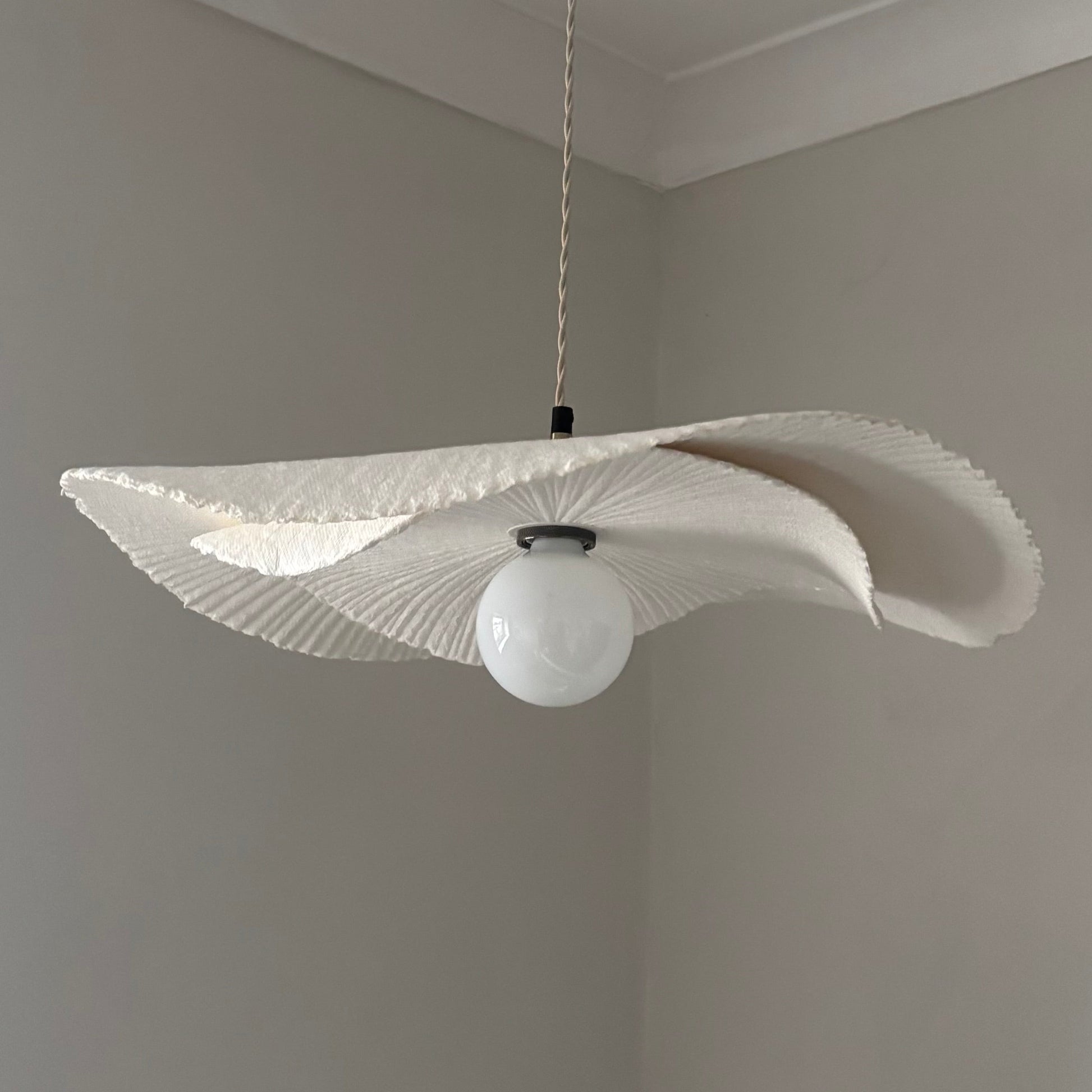 Modern pendant light with white lampshade and bulb against a plain wall