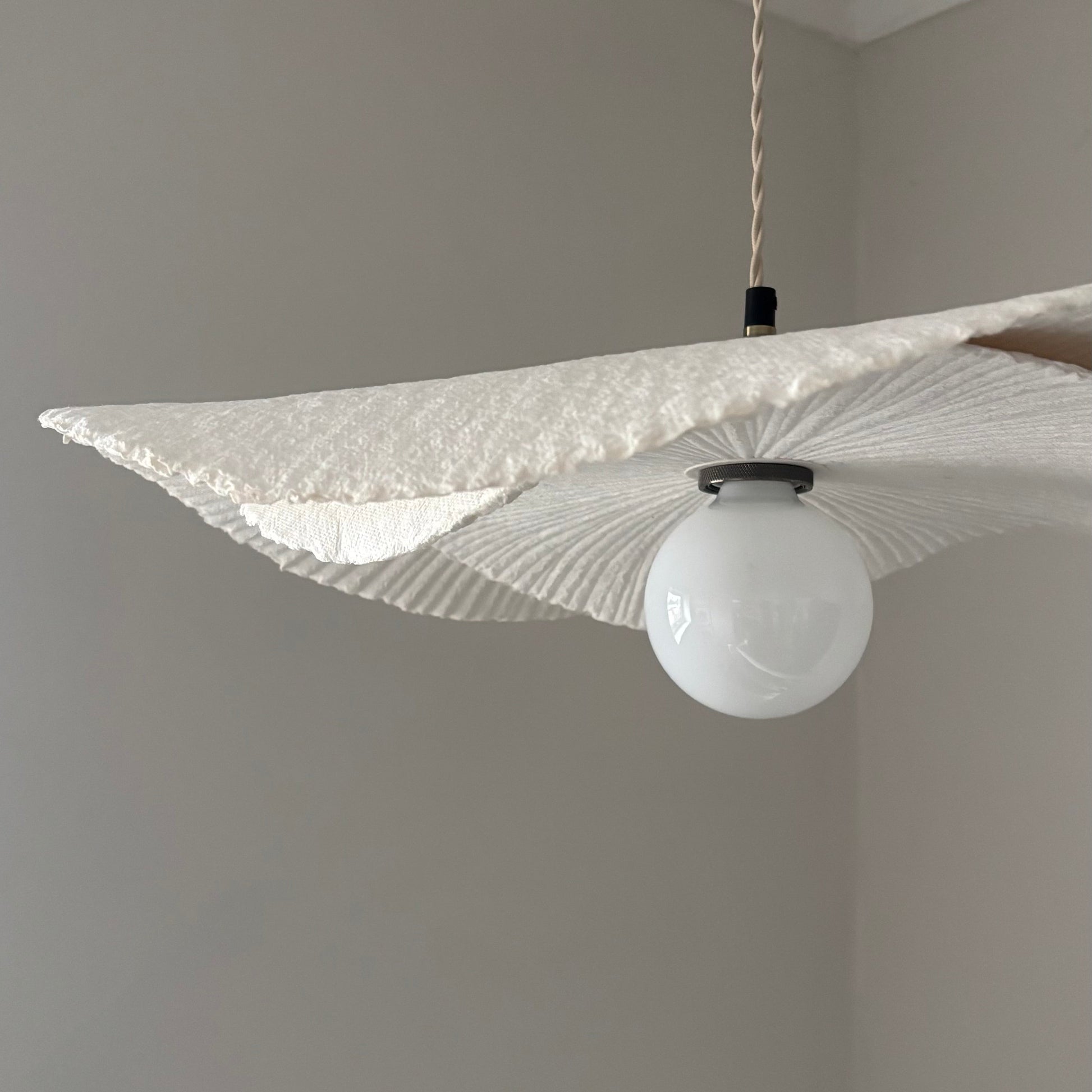 Modern pendant light with a textured shade on a neutral wall.
