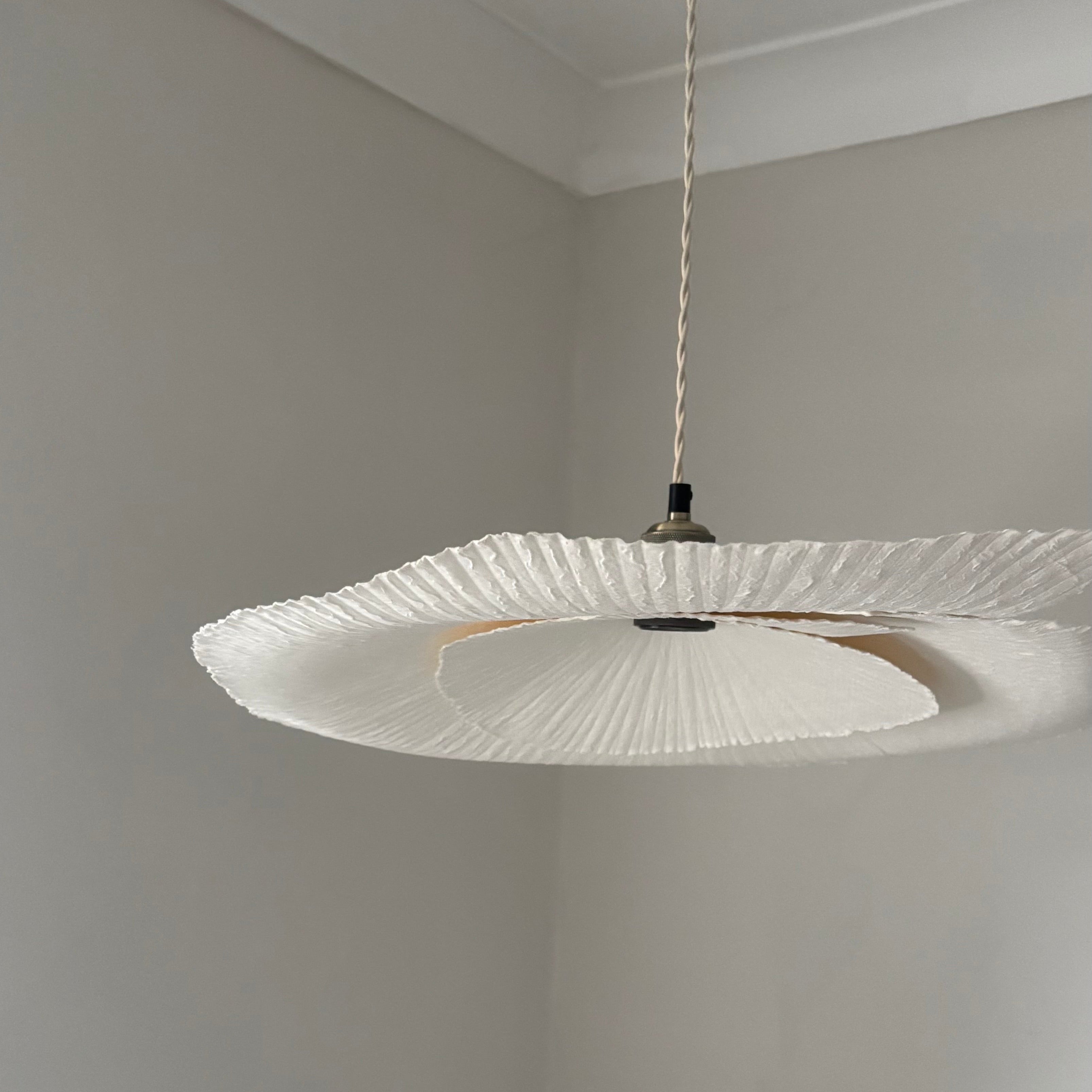 White pendant light fixture hanging from a ceiling in a room with gray walls.