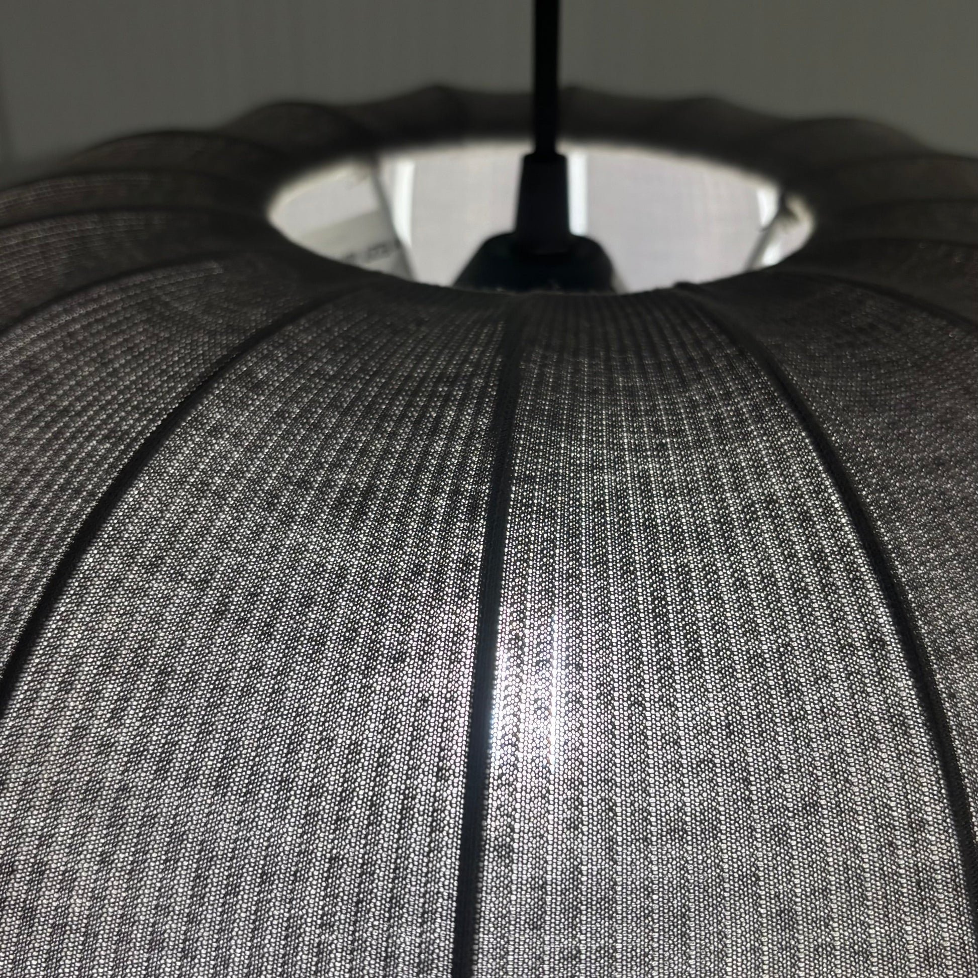 Close-up of a textured gray lampshade with a black cord against a neutral background