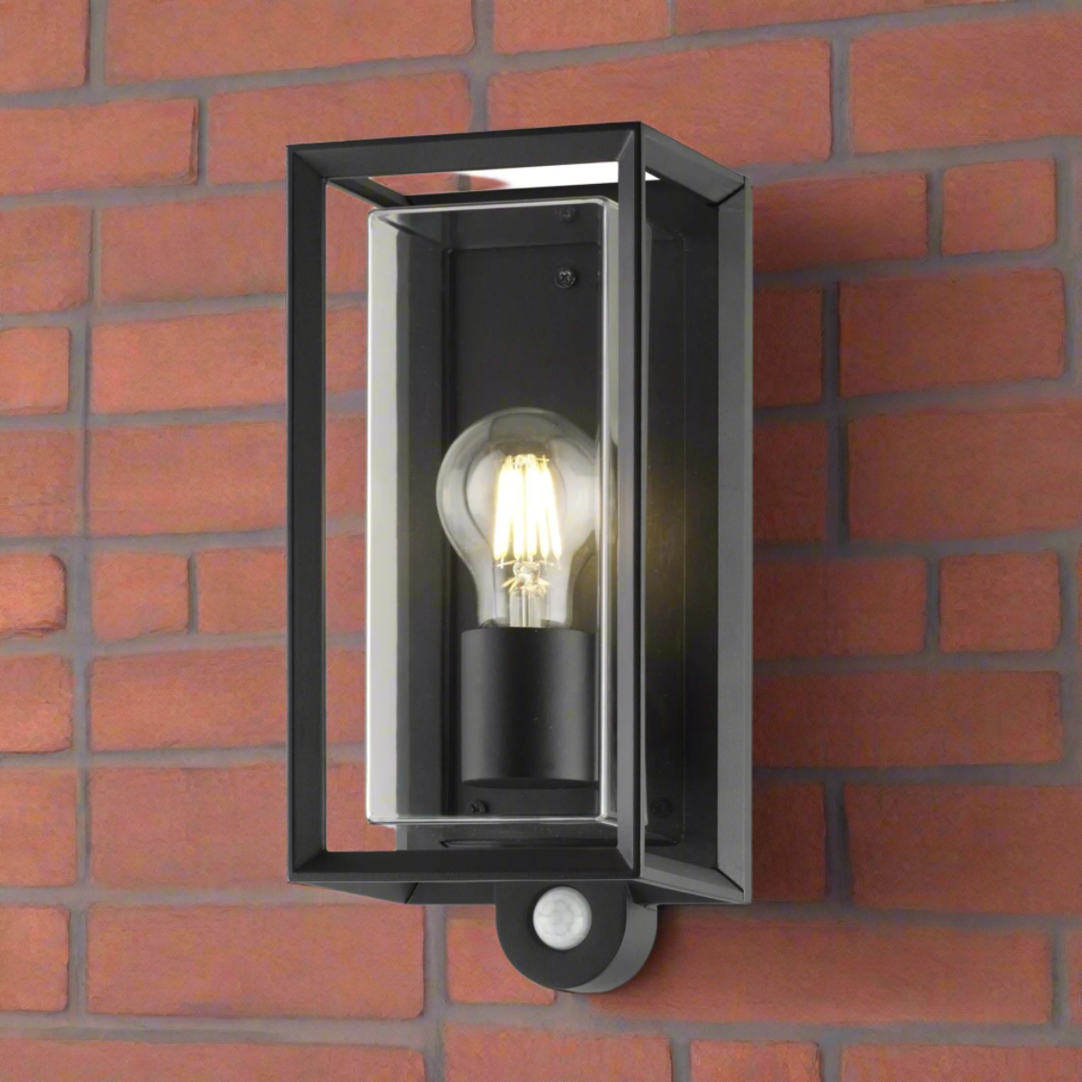 A black outdoor wall-mounted lantern with clear polycarbonate diffusers and a built-in PIR sensor, displayed against a brick wall background.