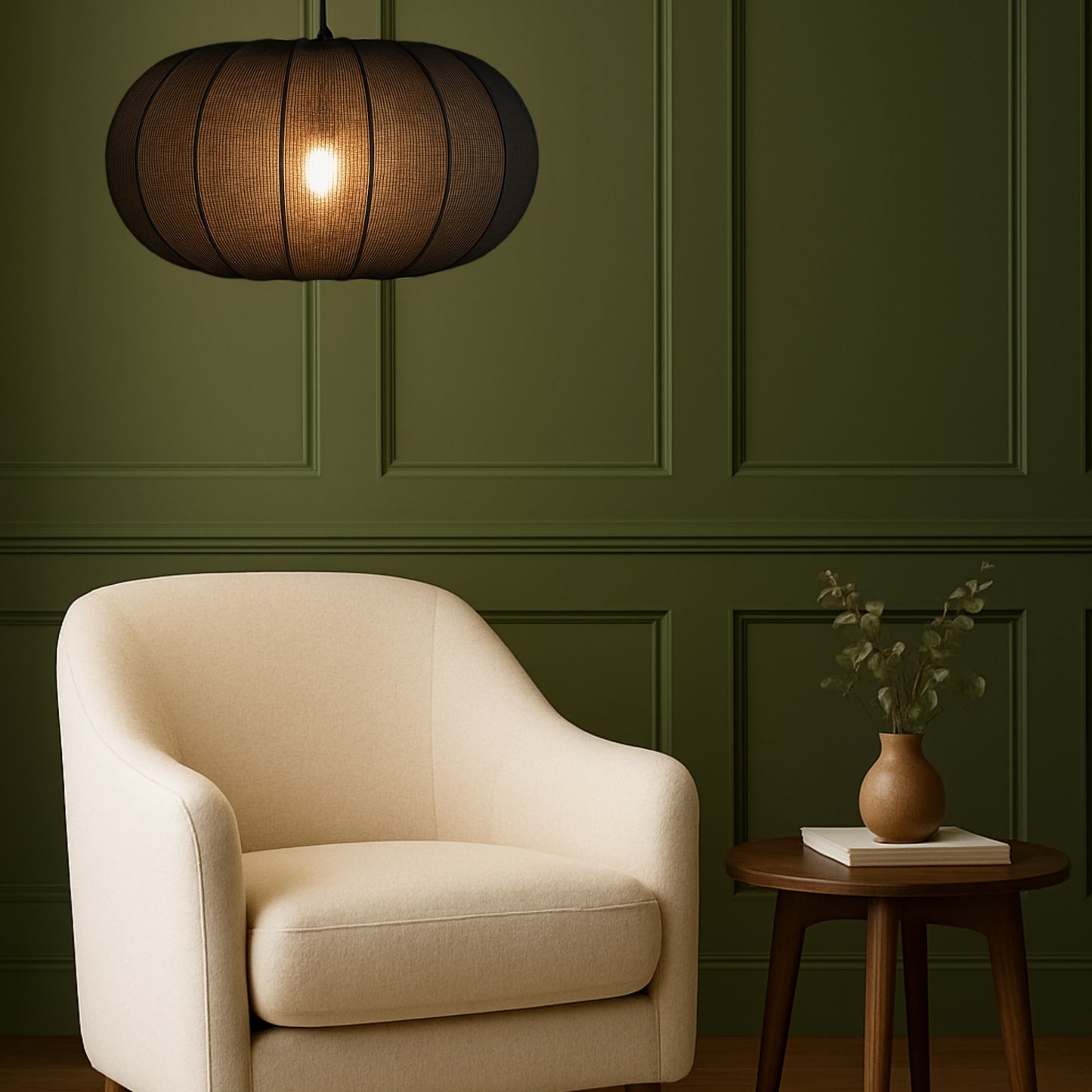 Beige armchair in a room with green paneled walls and a wooden side table with a vase and books.