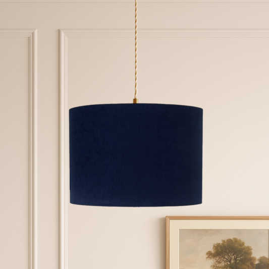 Navy blue lampshade hanging on a beige wall with a framed picture of a landscape.