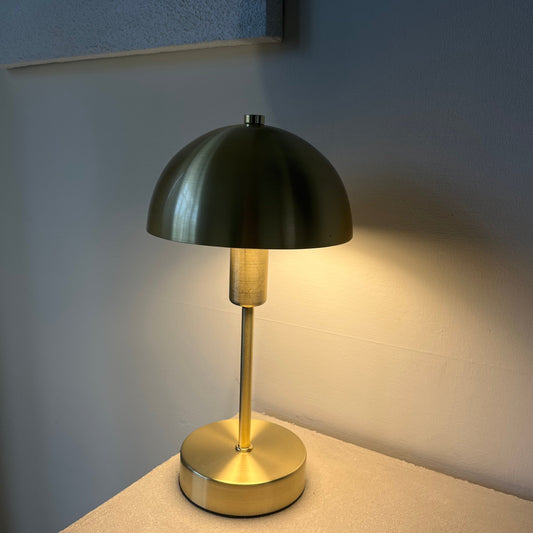 Introducing our Nellie table lamp with its distinctive dome-shaped shade and metal frame, this lamp will become a strong visual element in your space. Thanks to its gold matt antique metal finish, it will suit both modern and Mid-Century inspired settings. Light reflects off the shade to enhance a warm and inviting glow.