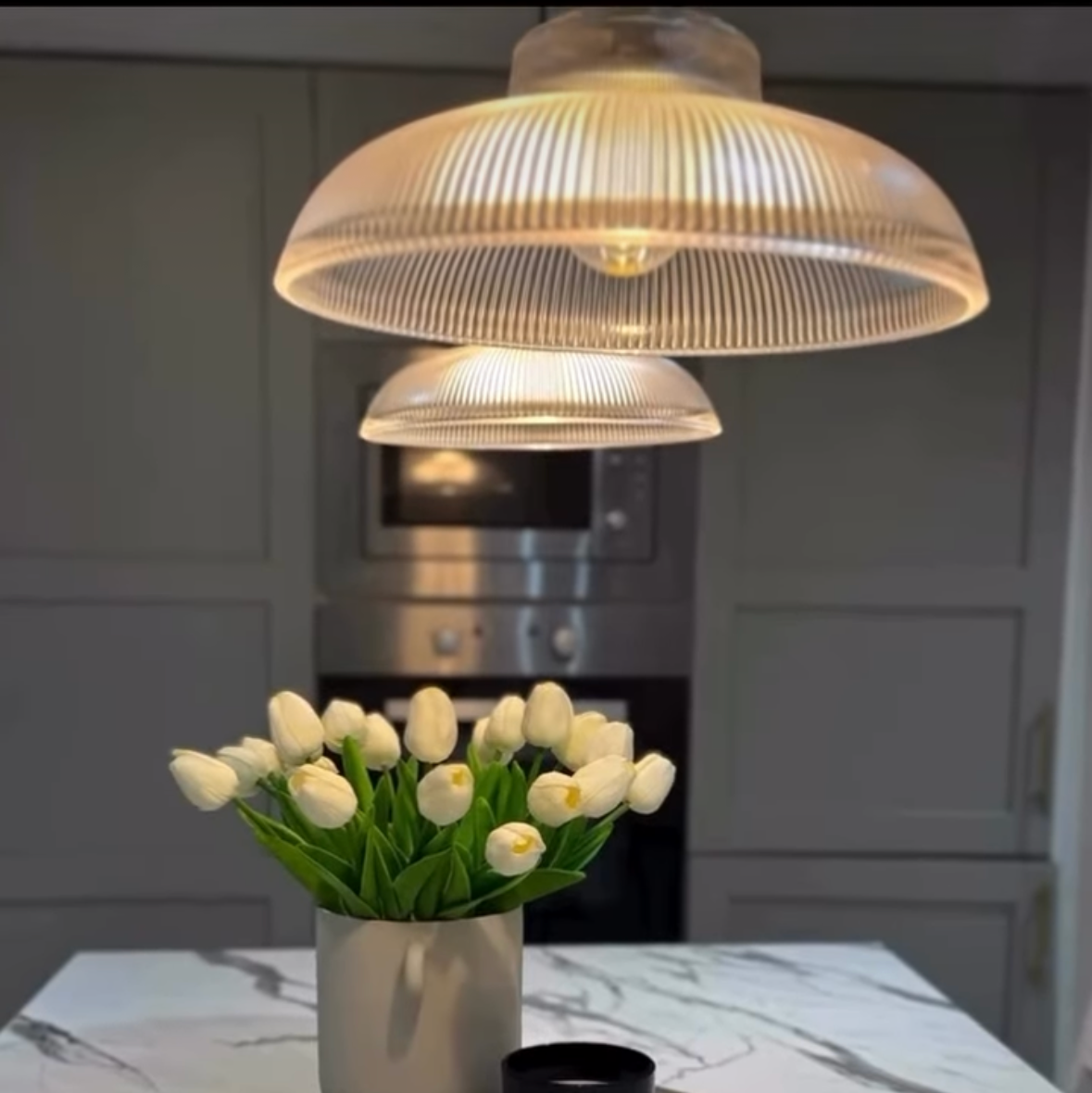 Decorative setup with a lamp, vase of tulips, and black mug on a marble surface.