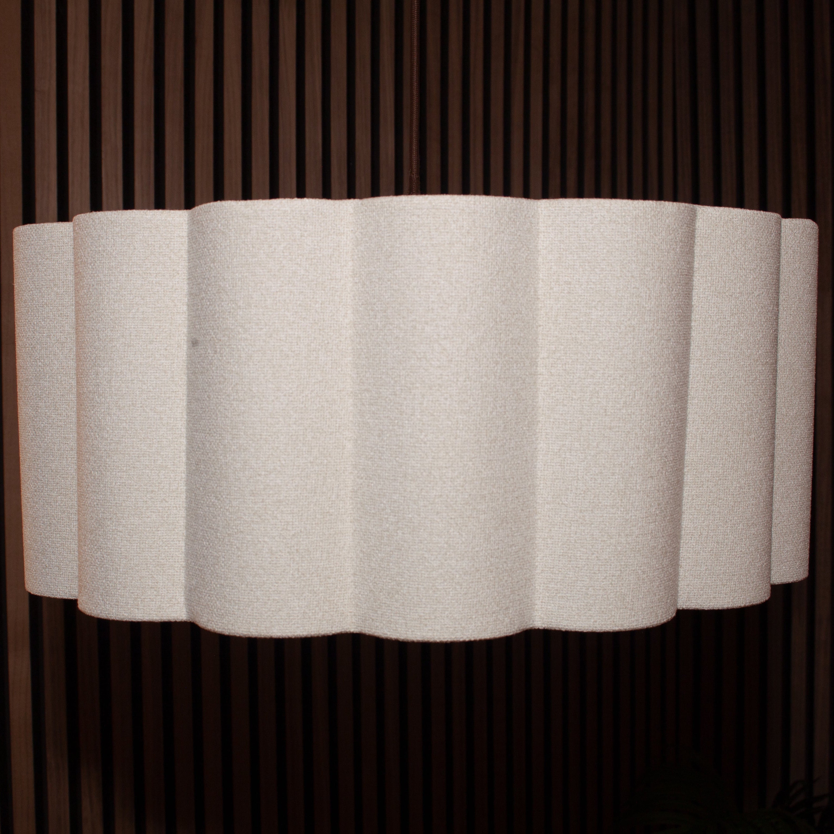 A modern wall sconce featuring a wavy, pleated white fabric shade mounted against a dark brown vertically slatted wooden wall.