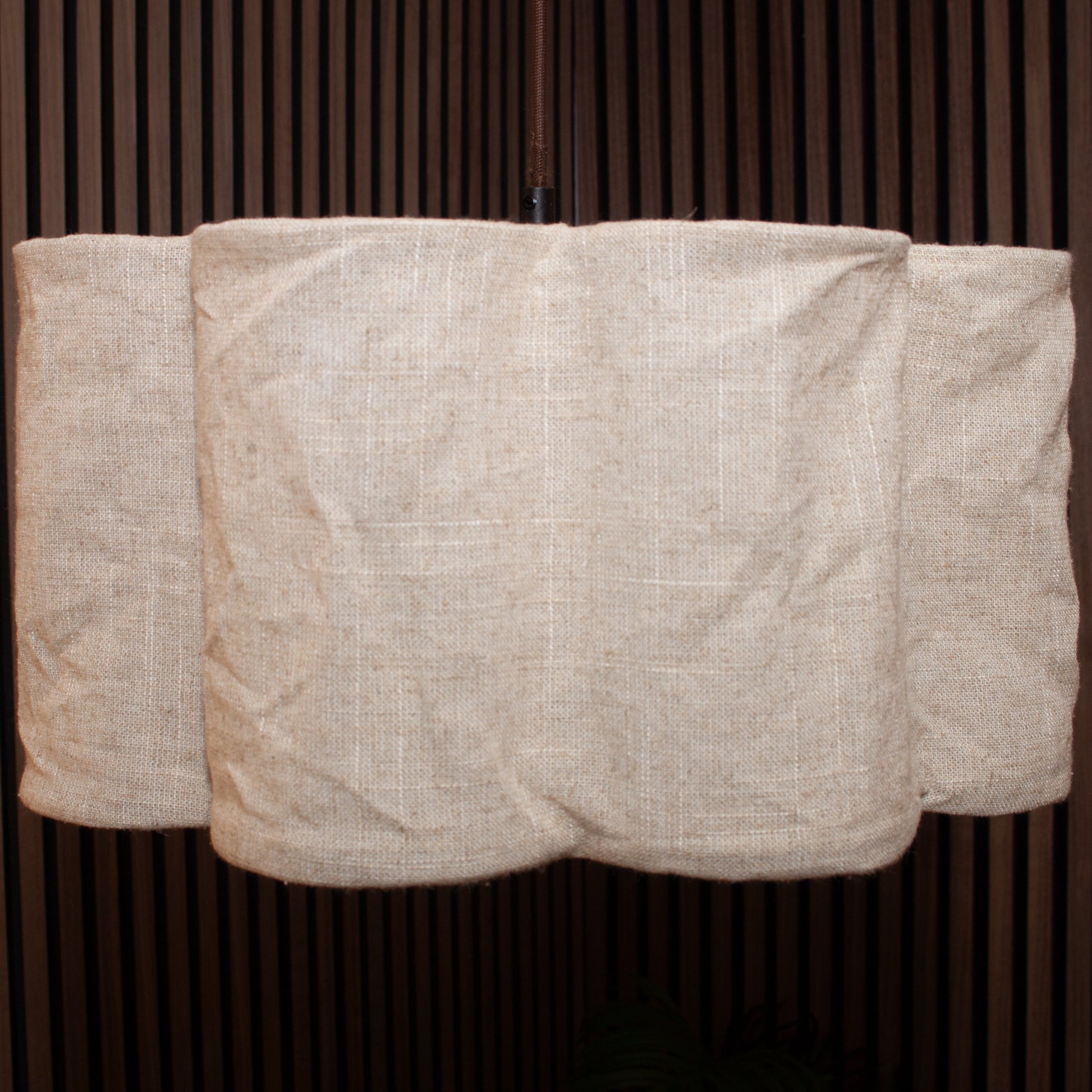 A light beige linen fabric cover draped over a cylindrical object, set against a dark brown vertically slatted background.