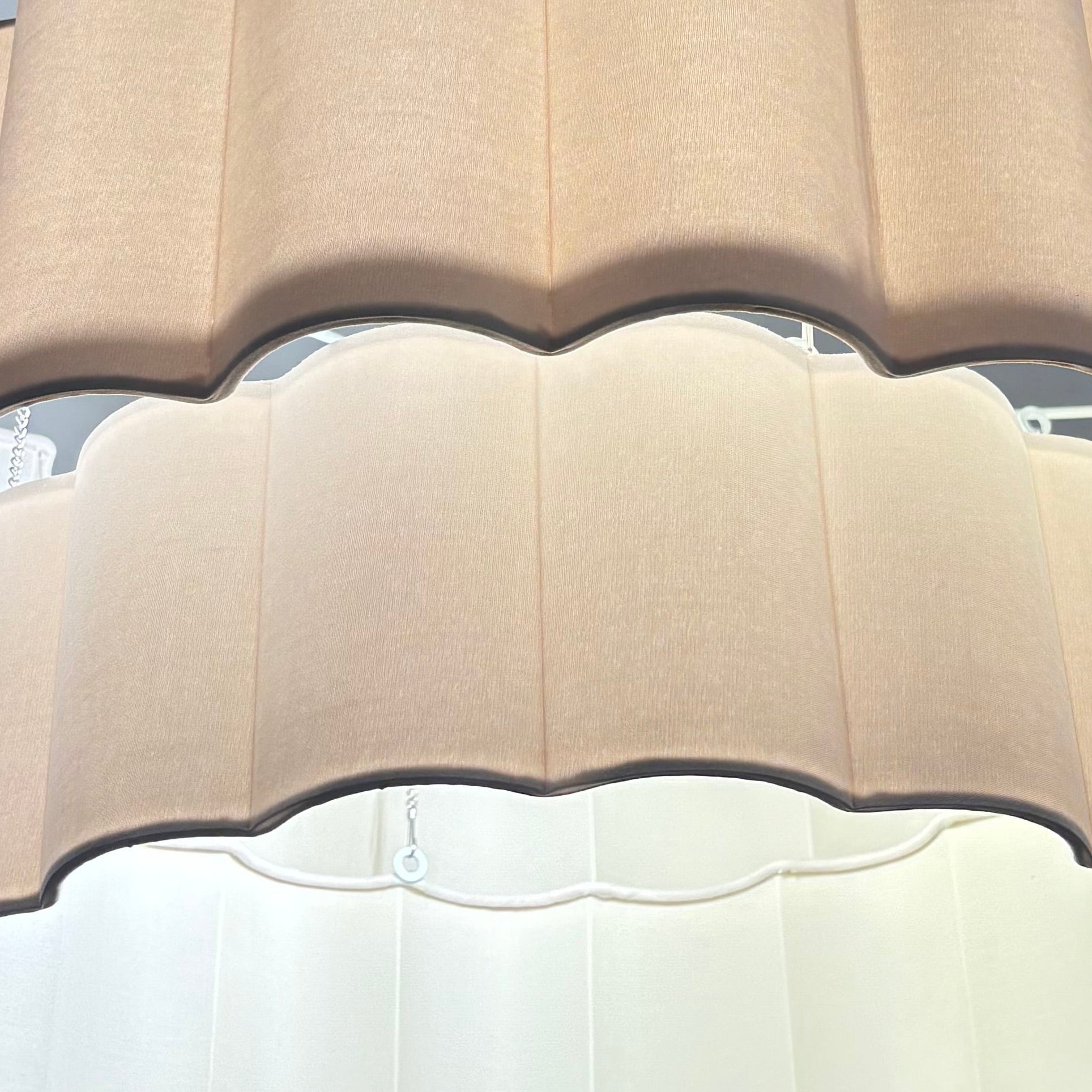 Beige scalloped-edge lampshade on a ceiling fixture against a gray wall.