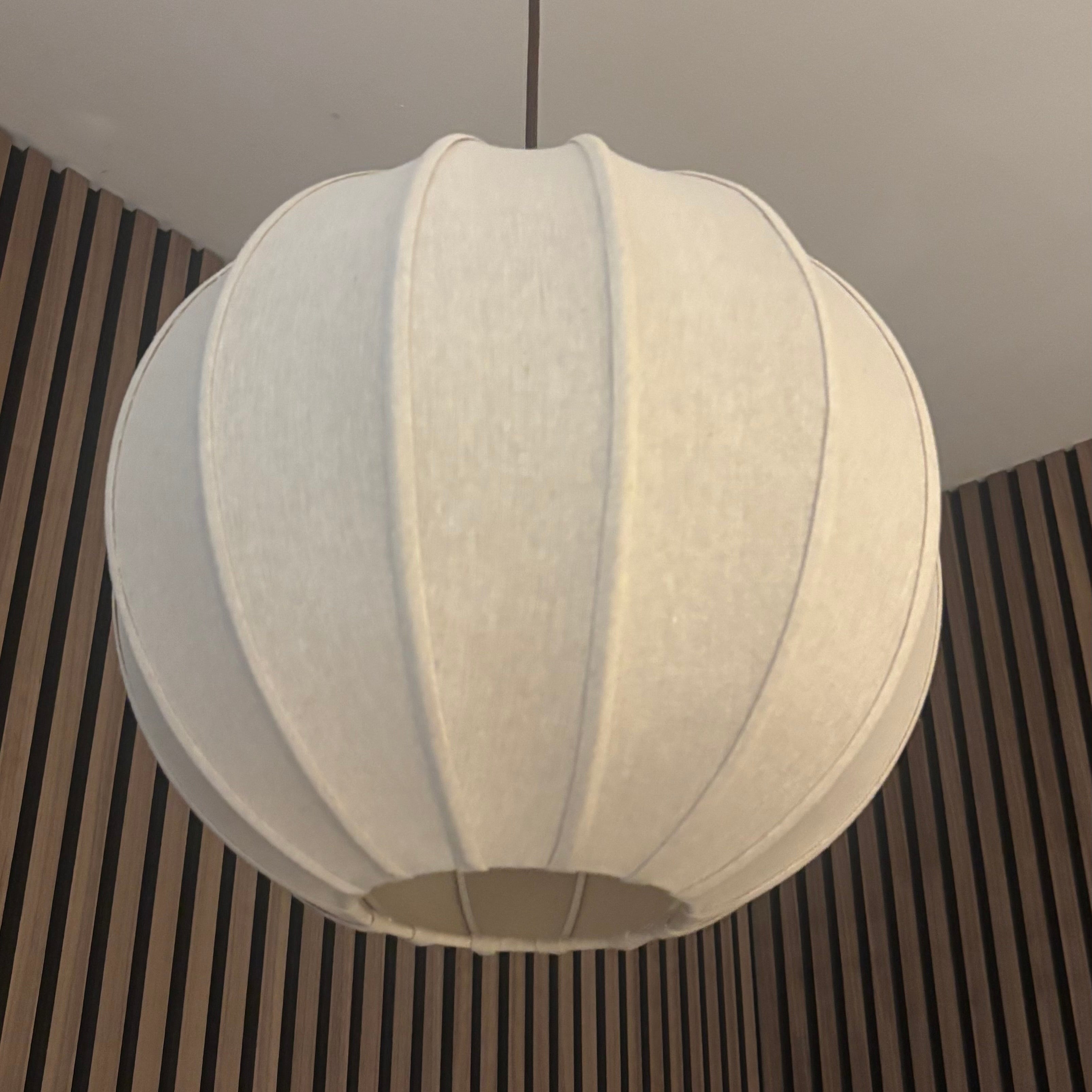 A spherical white fabric pendant light hanging from a ceiling in an indoor room with dark wood slat walls.