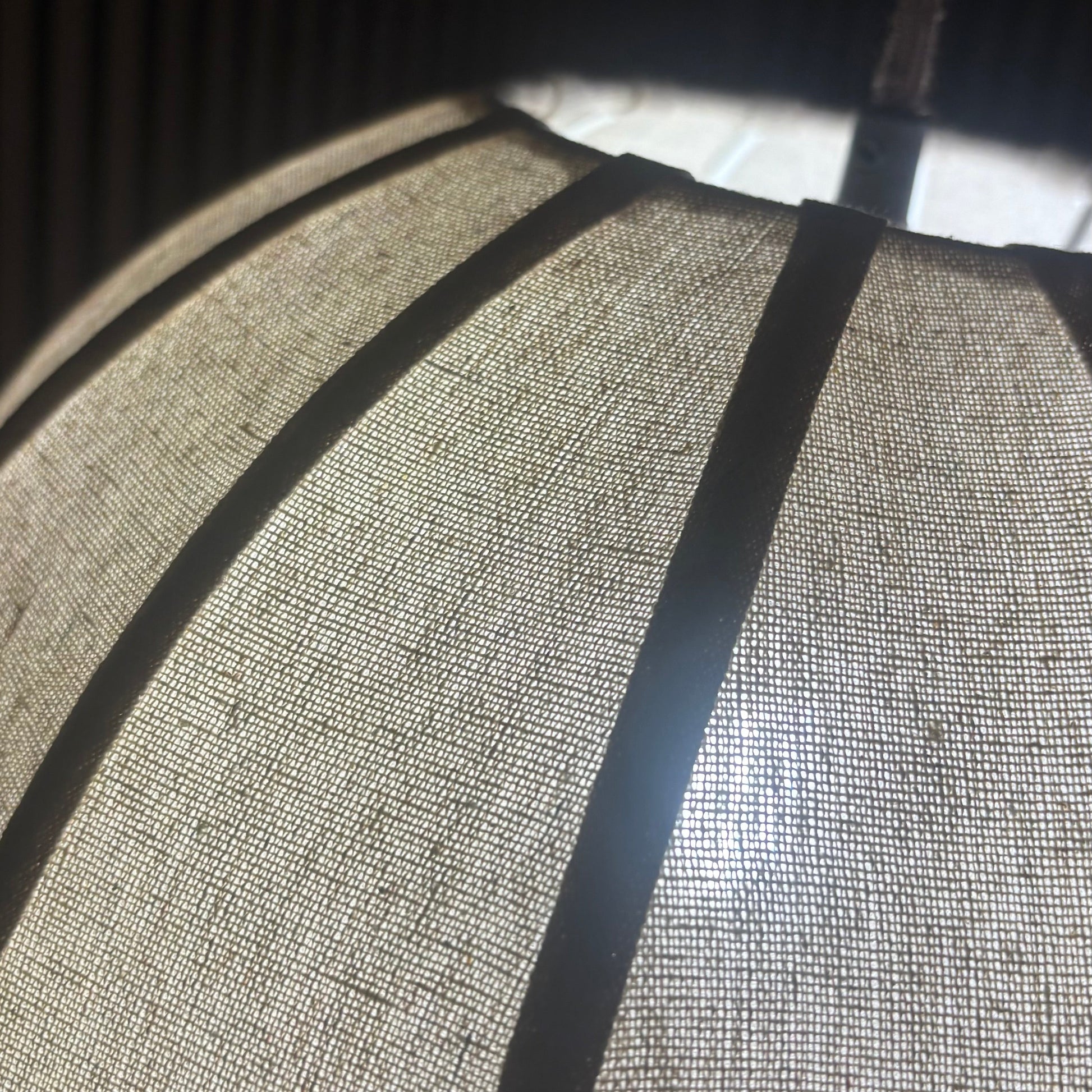 A close-up of a textured fabric lampshade with dark vertical bands, showing a woven linen-like pattern under warm light.