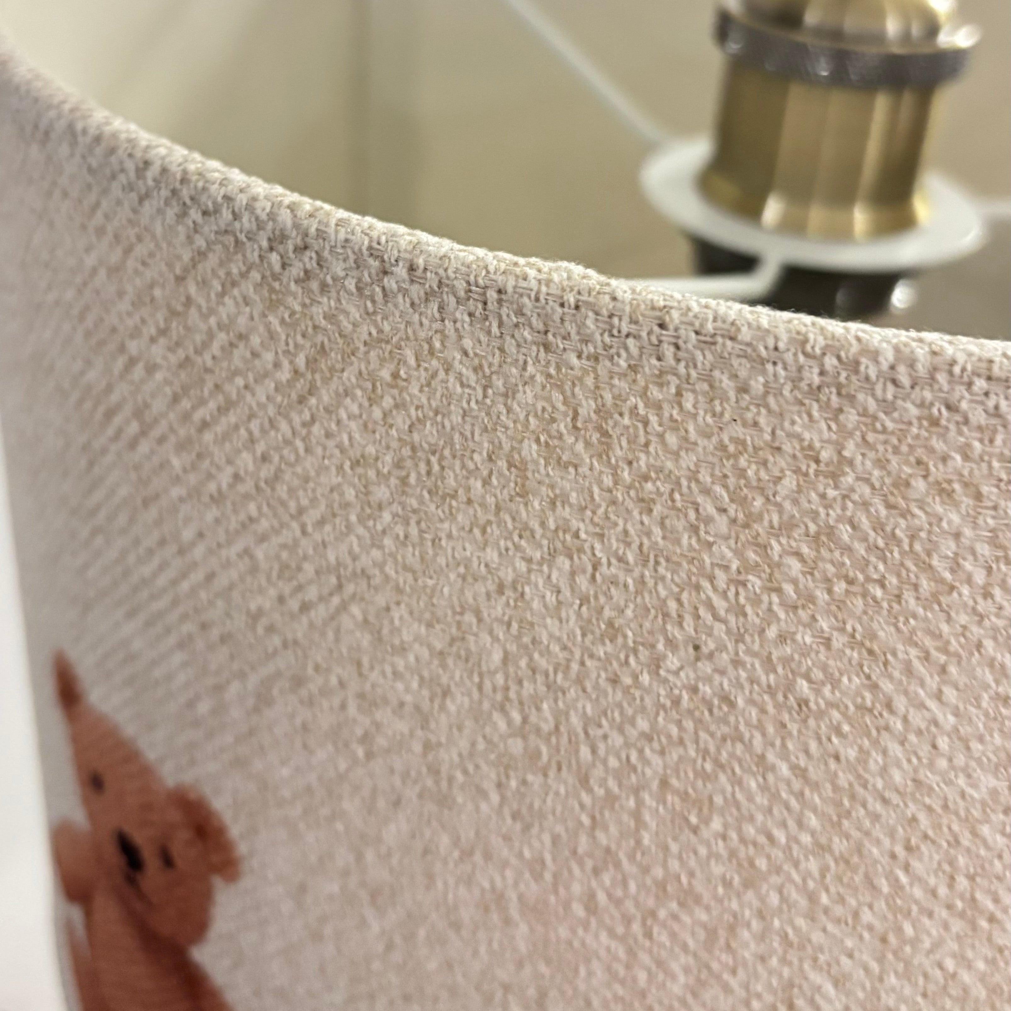 Close-up of a textured lampshade with a teddy bear design and a metallic fixture.