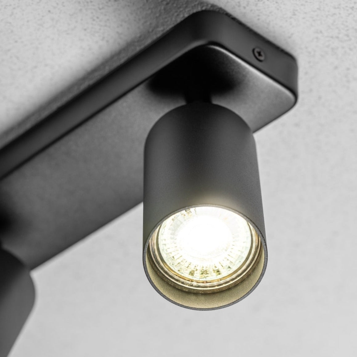 The black Nell twin lamp consists of two cylindrical spotlights, both of which can be tilted and adjusted on their own axis. The spotlights are attached to a rectangular bracket, which makes them equally suitable for mounting on walls and ceilings. Made of an aluminium body and powder coated black, the lamp with its simple design fits well into different spaces.