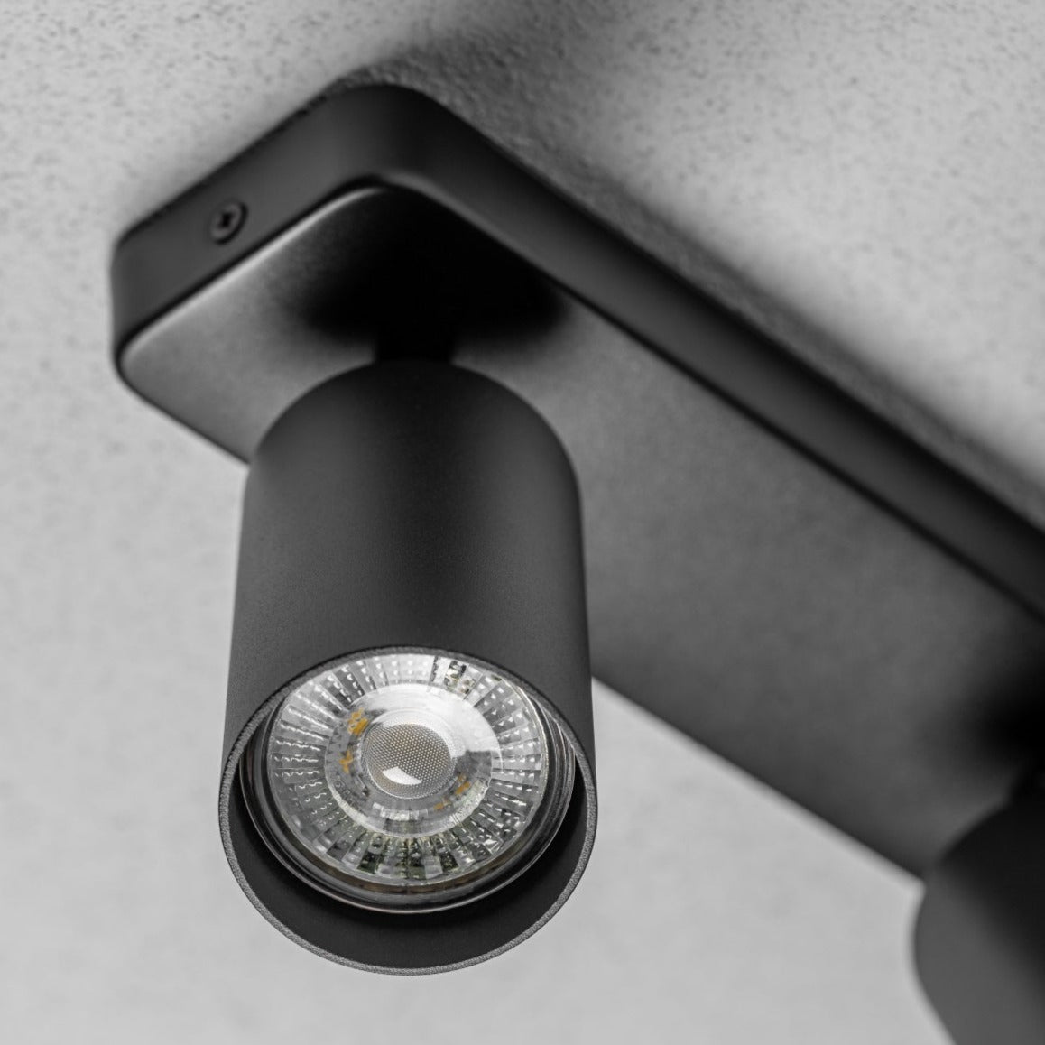 The black Nell twin lamp consists of two cylindrical spotlights, both of which can be tilted and adjusted on their own axis. The spotlights are attached to a rectangular bracket, which makes them equally suitable for mounting on walls and ceilings. Made of an aluminium body and powder coated black, the lamp with its simple design fits well into different spaces.