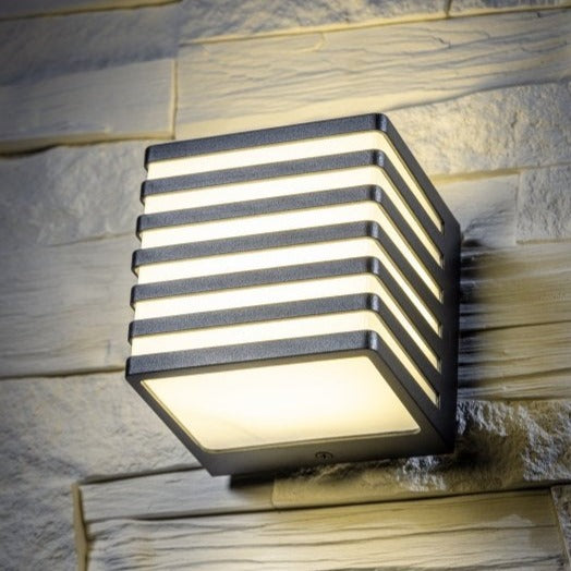 A black square LED outdoor cube wall light with a decorative grill, mounted on a wall.
