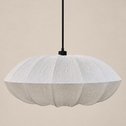A modern pendant light with a textured, pleated white shade in a scalloped, flower-like shape, suspended by a thin black cord against a solid beige background.