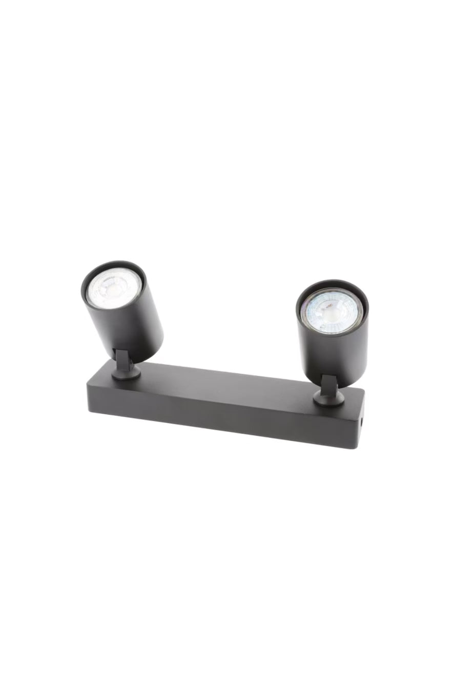 Load video: The black Nell twin lamp consists of two cylindrical spotlights, both of which can be tilted and adjusted on their own axis. The spotlights are attached to a rectangular bracket, which makes them equally suitable for mounting on walls and ceilings. Made of an aluminium body and powder coated black, the lamp with its simple design fits well into different spaces.