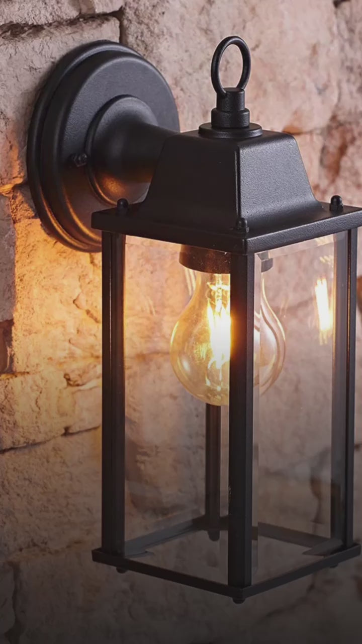 Load video: If you’re looking for a modern take on a traditional outdoor wall light, this glass coach wall light is perfect for adding style and protection for your home. This classic lantern light is designed with a contemporary twist, styled with a cuboid shape and fitted with glass windows that allow the light to shine effectively. 