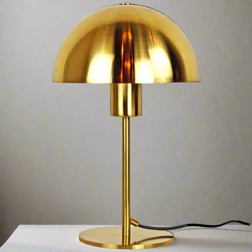 Our Kelly table lamp is a strong visual addition to your space with its distinctive dome-shaped shade and metal frame. Thanks to its brushed gold brass metal finish, it will suit both modern and Mid-Century inspired settings. Light reflects off the shade to enhance a warm and inviting glow.