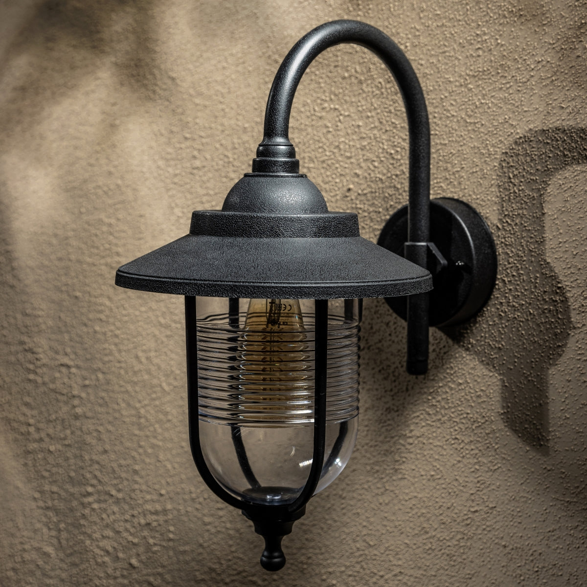 The Jemima black fisherman hooked outdoor wall lantern light is constructed of polycarbonate and features an attractive design inspired by traditional lighting styles. This lantern wall light is a great choice for illuminating doorways and porches, creating a warm and inviting look and a safe environment. With an IP44 safety rating, the Jemima garden wall light is suitable for mounting on outdoor walls.