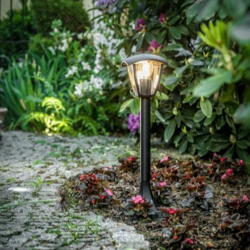 Solar garden light on a stone path with greenery and flowers in the background